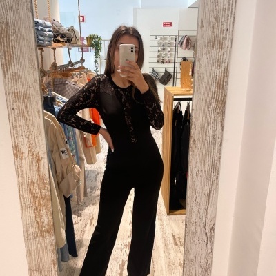 Mulher a tirar foto no espelho usando macacão preto com mangas de renda.