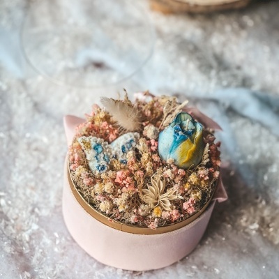 Caixa redonda rosa com arranjo seco de flores e vela decorativa azul amarela
