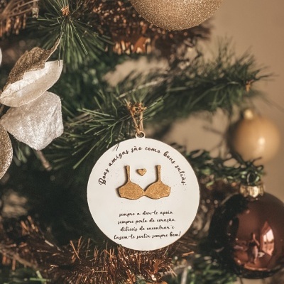 Enfeite de Natal redondo branco com relevo dourado de soutien e texto sobre amizade pendurado em árvore de Natal decorada