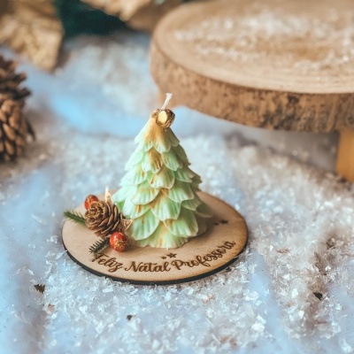 Vela árvore de Natal verde com sino dourado numa base de madeira com texto 'Feliz Natal Professora' sobre neve artificial