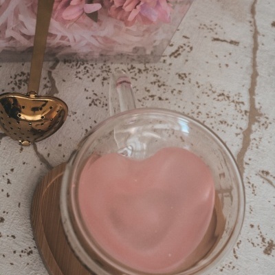 Chaleira de vidro com infusor rosa em forma de coração sobre base de madeira e colher de chá com coração