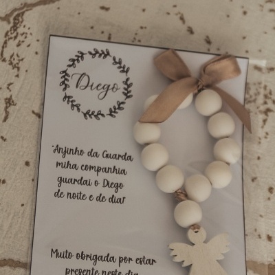 Anjo da guarda decorativo com contas brancas e laço castanho num cartão com texto em português