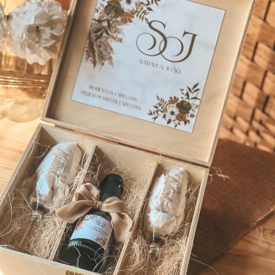 Caixa de madeira com garrafa de vinho, duas flûtes decoradas e cartão floral