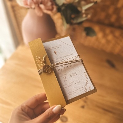 Convite de papel com envelope castanho claro e cordão rústico, texto em português com data setembro 2026, sobre mesa de madeira com vaso de flores ao fundo