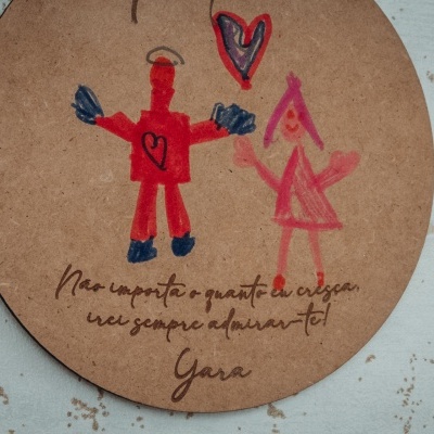 Placa redonda em madeira com desenho de bonecos e texto manuscrito em português.