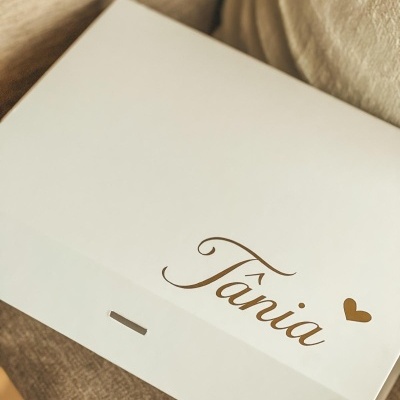 Caixa branca com nome Tânia em dourado e coração, sobre tecido castanho claro