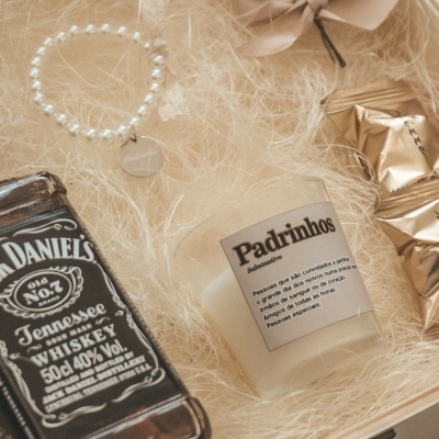 Conjunto de presente com garrafa de whiskey Jack Daniel's, pulseira prateada, vela com texto Padrinhos e bombons dourados numa caixa de madeira