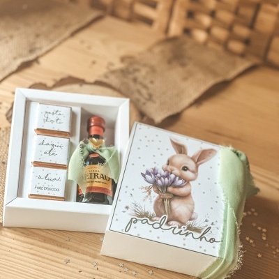 Conjunto oferta com caixa ilustrada de coelho, garrafa de licor e chocolates embalados em papel branco com texto em português.