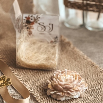 Vela em forma de flor bege creme sobre juta com caixa transparente e fita bege.