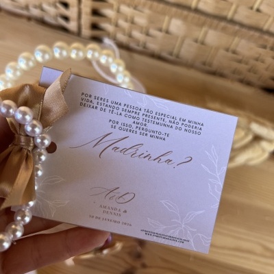 Cartão de convite com pulseiras de pérolas e saco de tecido castanho claro sobre mesa de madeira clara