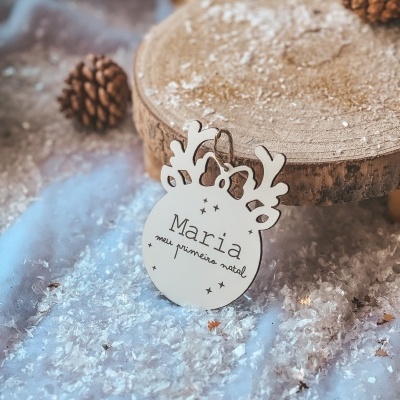 Decoração de Natal branca em madeira com texto personalizado, rodeada de neve artificial e pinhas.