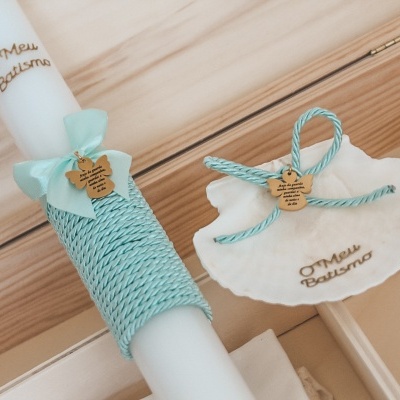 Vela branca decorada para batismo com corda azul turquesa e acessório em forma de concha numa caixa de madeira