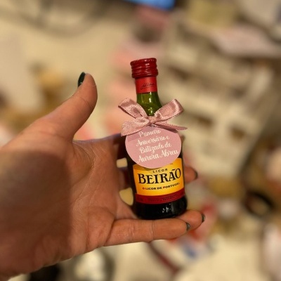 Pequena garrafa de Licor Beirão com laço rosa e etiqueta comemorativa em mão