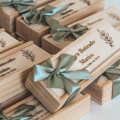 Caixas de madeira claras com laços verdes e gravação para batizado