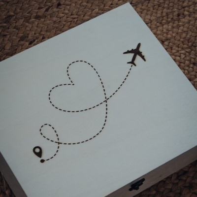 Caixa de madeira clara com avião e linha pontilhada formando um coração