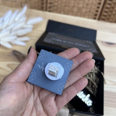 Embalagem cinza com broche em mão sobre fundo com caixa preta aberta e decoração