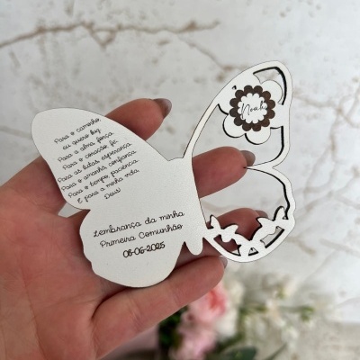 Cartão em forma de borboleta com texto sobre Primeira Comunhão, segurado por mão com unhas castanho claro