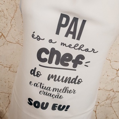 Avental branco com texto em preto sobre parede bege rachada