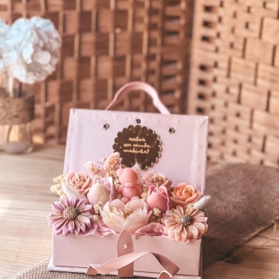 Arranjo decorativo com flores artificiais e vela ursinho cor-de-rosa numa caixa rosa