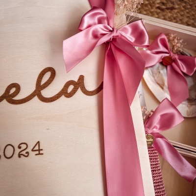 Caixa de madeira clara com fita rosa em cetim e flores secas em fundo de tecido castanho