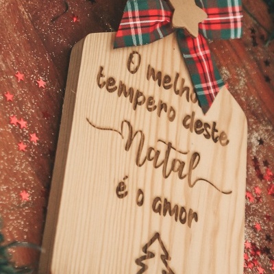 Tábua de madeira clara decorada com fita tartan e mensagem gravada 'O melhor tempero deste Natal é o amor'