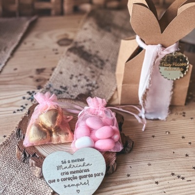 Saquinhos de organza com chocolates, placa de madeira em forma de coração com texto e embalagem de papel castanho com orelhas de coelho numa mesa de madeira.