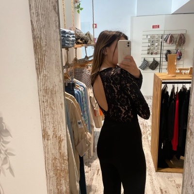 Mulher a experimentar macacão preto com renda nas costas, tirando foto em espelho numa loja de roupas.