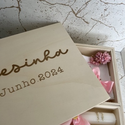 Caixa de madeira clara com gravação e itens decorativos cor de rosa dentro