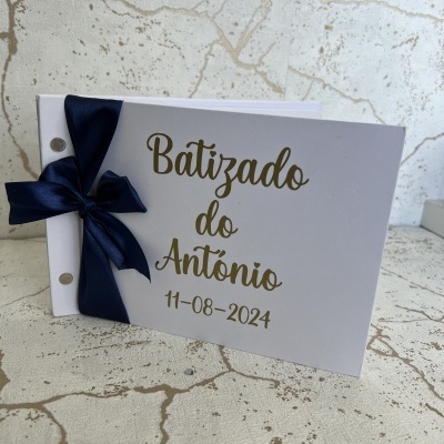 Livro de batizado branco com texto dourado e laço azul escuro