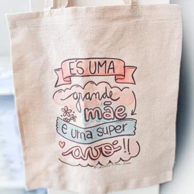 Mala de tecido cru com texto colorido em português sobre mãe e avó
