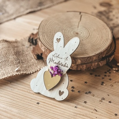 Objeto decorativo de madeira em forma de coelho com texto e flores secas.