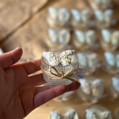 Recipiente de vidro com borboleta em cerâmica azul com flores amarelas, decorado com corda e etiqueta, em fundo de mesa com mais recipientes semelhantes