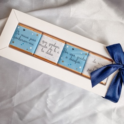 Caixa branca com barra de chocolate embalada e laço azul