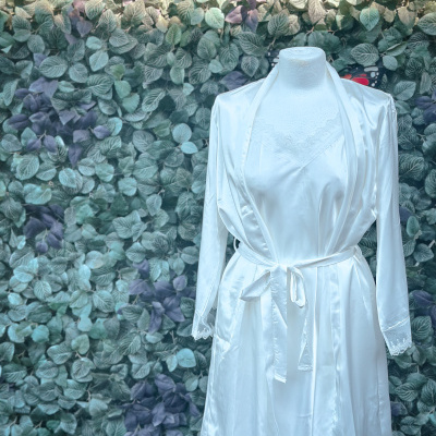 Vestido de cetim branco com renda em manequim em frente a parede de folhas.