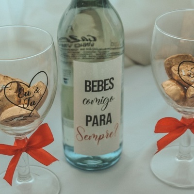 Garrafa de vidro com etiqueta e duas taças de vidro com laços vermelhos, cada uma com duas rolhas dentro