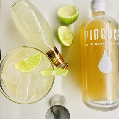 Bebidas com garrafa PIOGUCA, copo com gelo e fatias de lima, meia lima cortada.