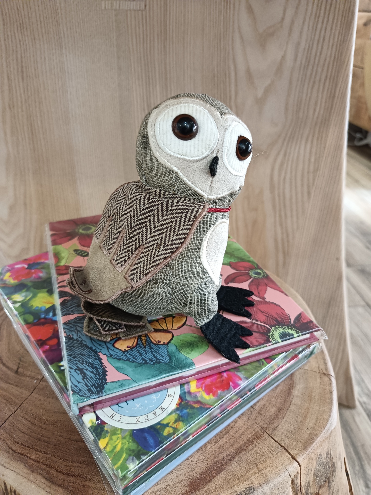 Pisa-Papéis Barn Owl Junior - Mocho Boneco coruja tecido em cima de caixas com capas florais sobre mesa de madeira