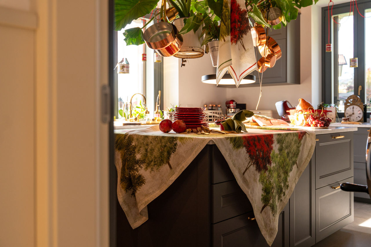 Toalha de Mesa 100% Linho GREESON- Tessitura Toalha de mesa com padrão verde e vermelho sobre bancada de cozinha cinzenta com elementos decorativos.