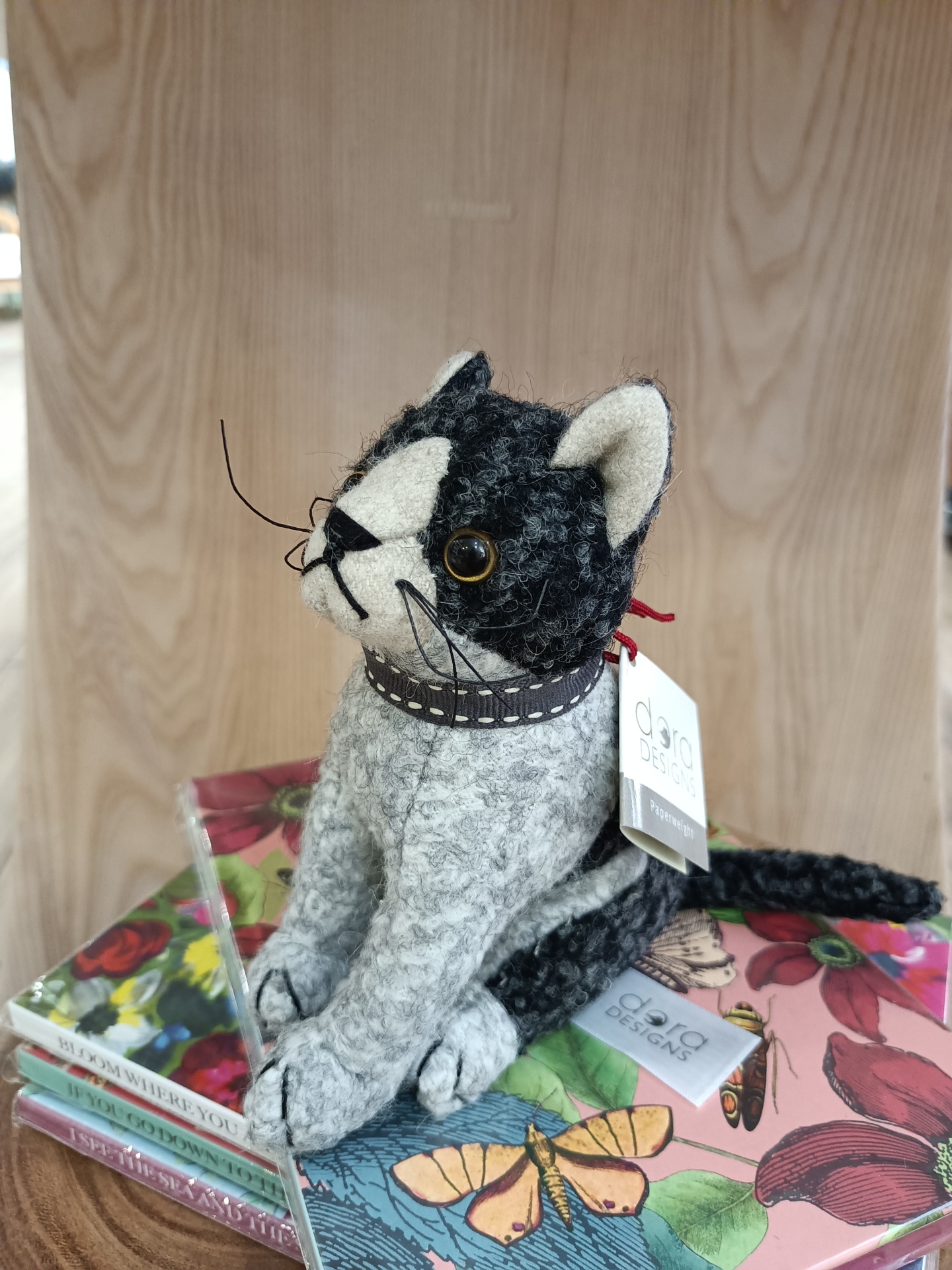 Pisa-Papéis Pepe Junior - Gato Boneco decorativo de gato em tecido cinzento e preto sobre livros coloridos com capa ilustrada.