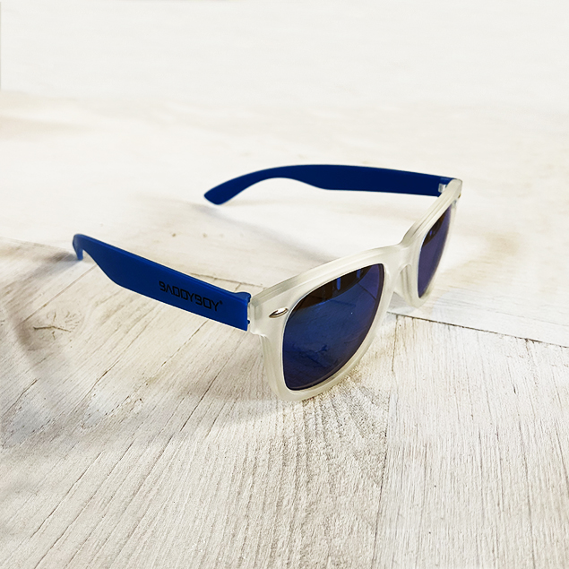 BADDYBOY - ÓCULOS DE SOL ROME Óculos de sol com armação transparente e hastes azuis em superfície de madeira clara