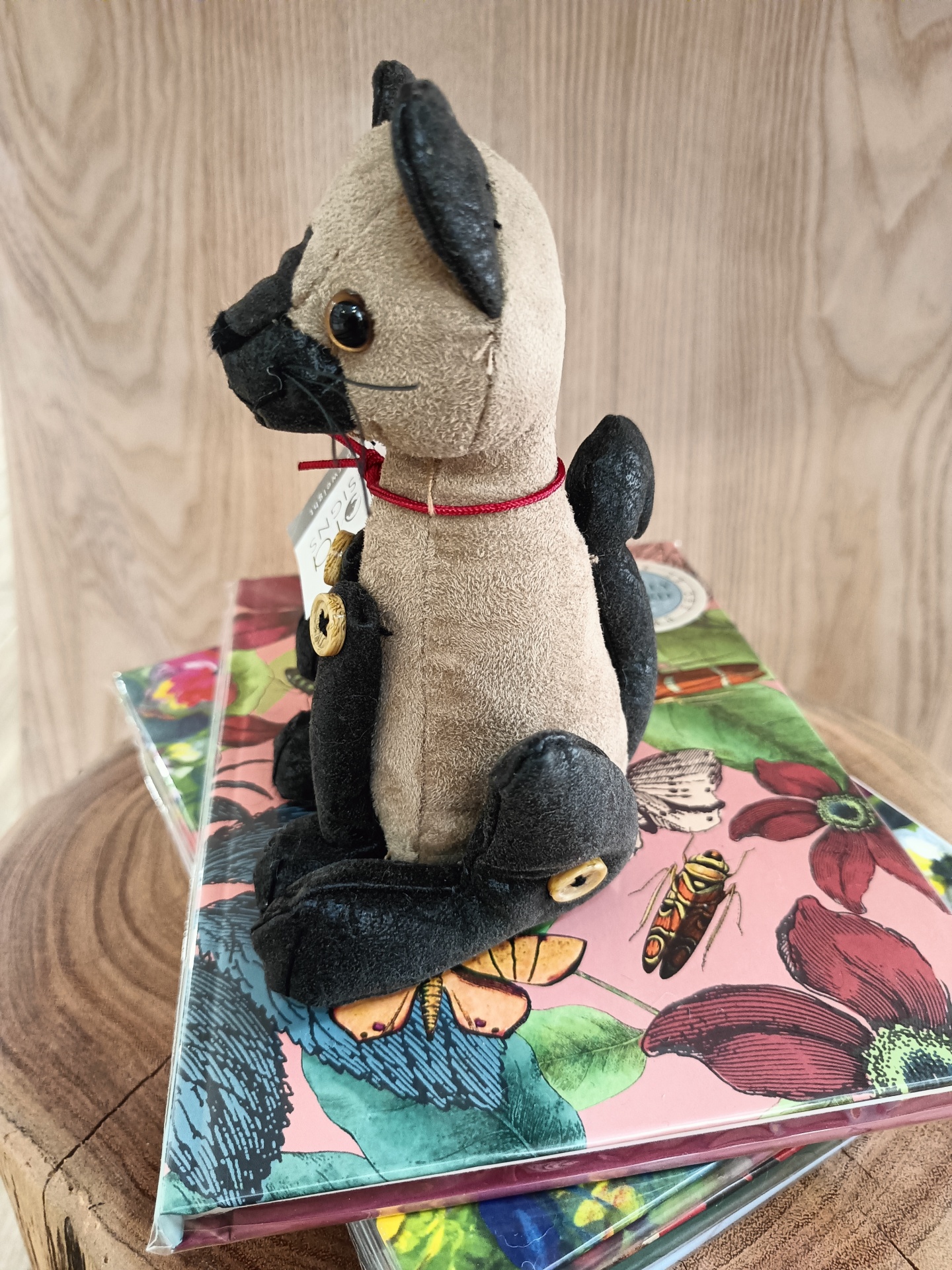 Pisa-Papéis Slinky Junior - Gato Boneco de peluche de cão com detalhes pretos sentado sobre agendas floridas sobre madeira