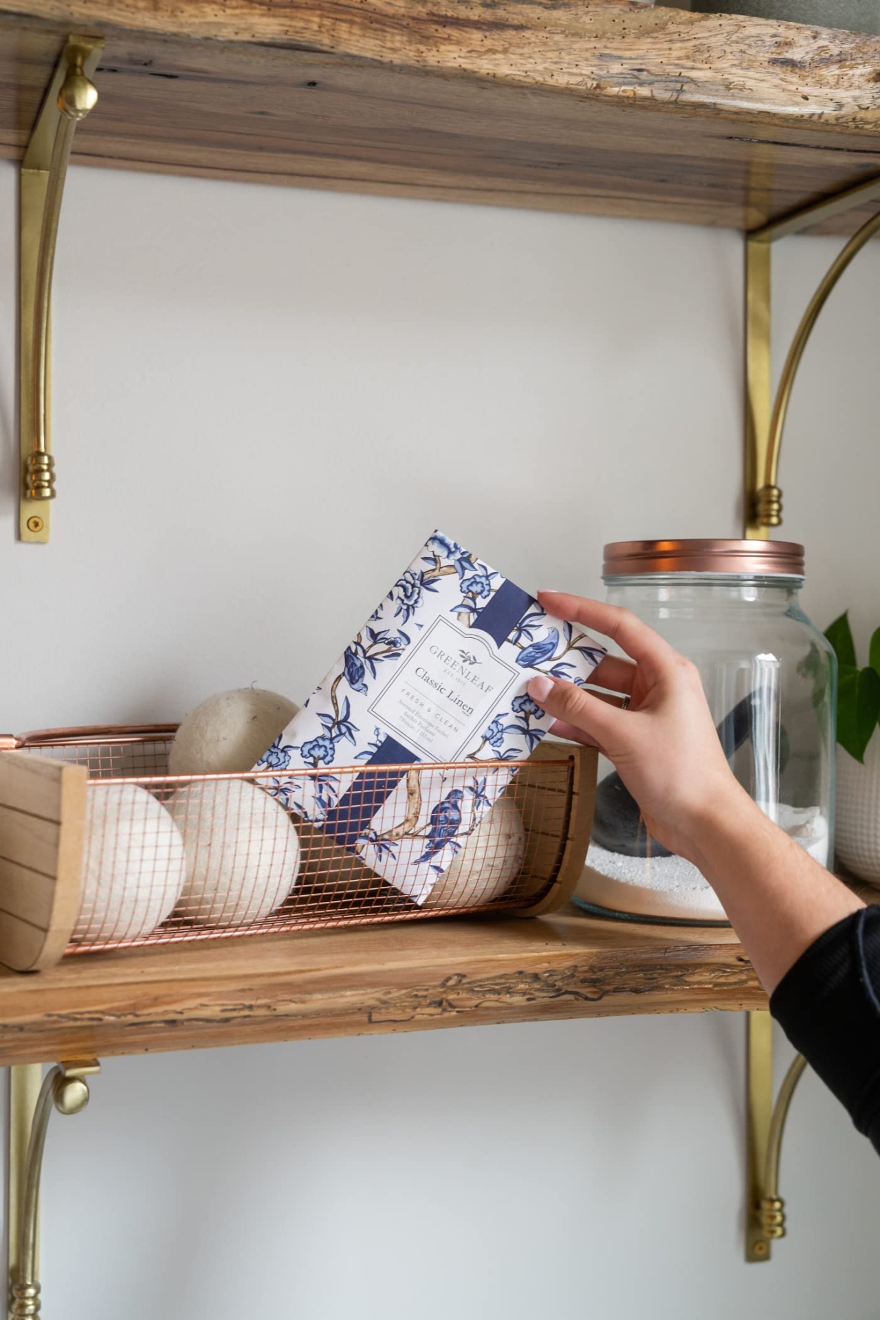 Mão segurando pacote floral azul e branco em prateleira de madeira