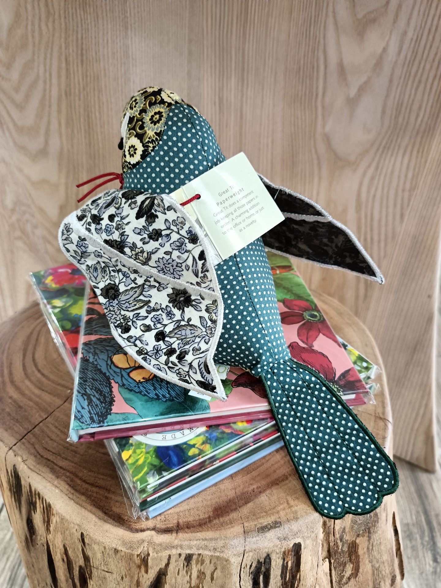 Pisa-Papéis Great Tit - Passarinho Boneco tecido em forma de pássaro colorido sobre cadernos coloridos num tronco de madeira