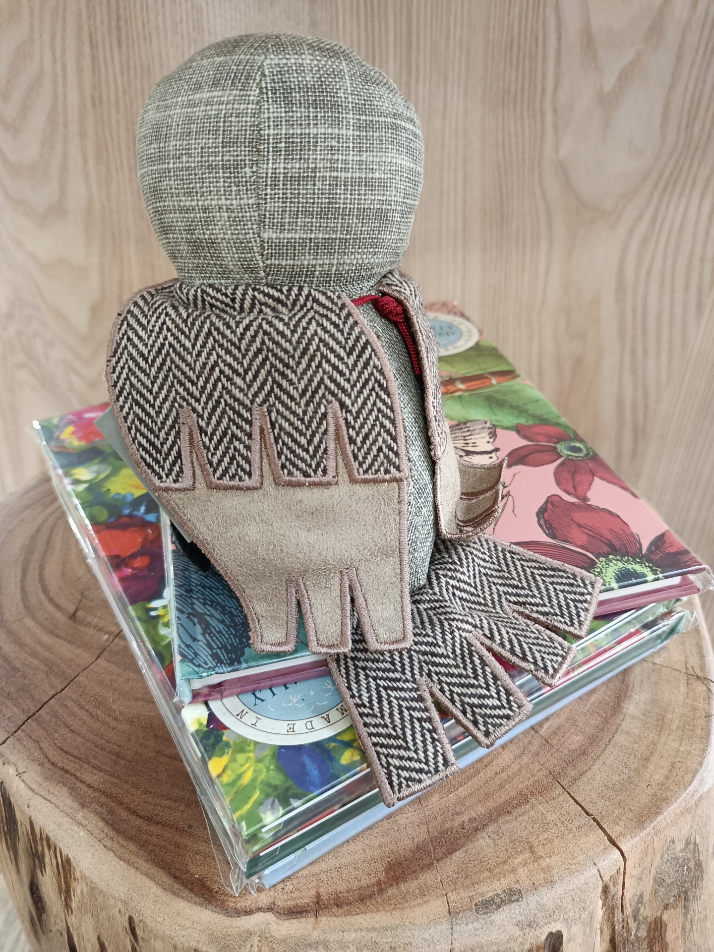 Pisa-Papéis Barn Owl Junior - Mocho Boneco de tecido cinzento e bege sentado sobre livros coloridos numa superfície de madeira