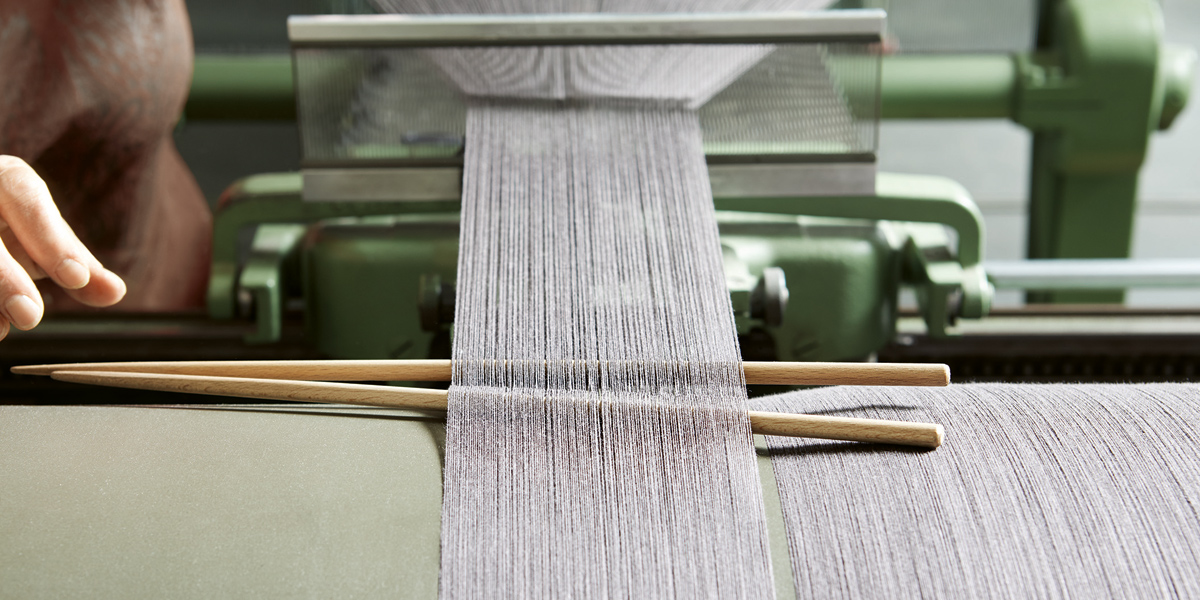 Máquina de tecer fios cinzentos com varas de madeira e mão ajustando