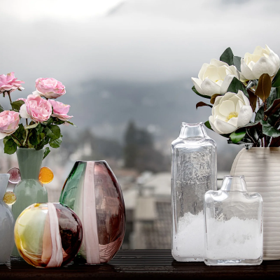 Vasos de vidro com flores artificiais rosas e brancas sobre superfície escura