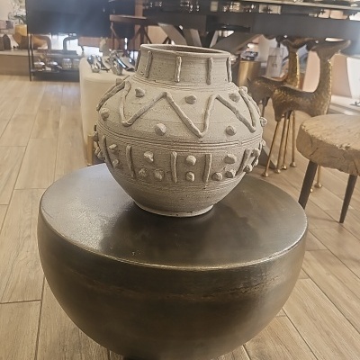 Vaso cinza de cerâmica com padrão geométrico sobre banco preto em loja de decoração