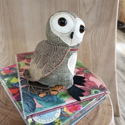 Boneco coruja tecido em cima de caixas com capas florais sobre mesa de madeira