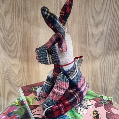 Urso de peluche xadrez sentado sobre livros coloridos, fundo madeira clara