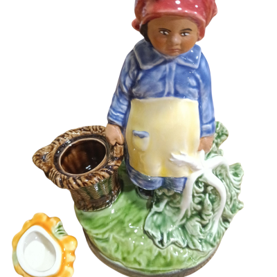 Figura decorativa em porcelana de mulher vestida em azul e amarelo com lenço vermelho, segurando uma cesta, sobre base verde com tigela amarela ao lado